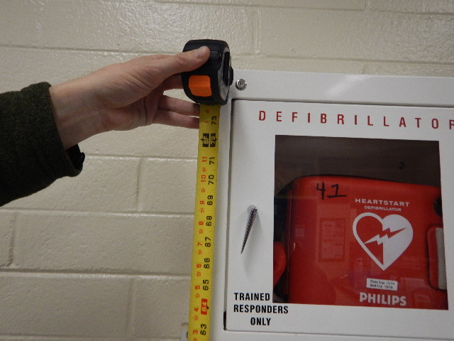 Accessibility specialist measuring height of defibrillator box on wall
